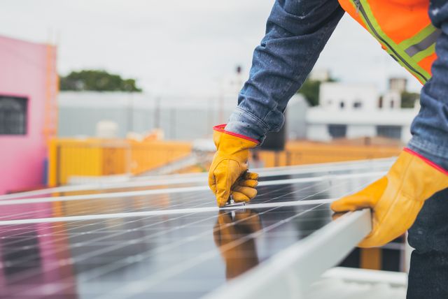 Ruke u zaštitnim rukavicama zatežu vijak na solarnom panelu