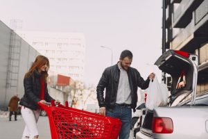 Muškarac i žena stavljaju kese iz crvenih kolica u gepek automobila
