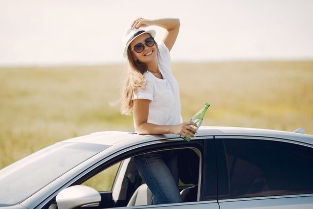 Žena drži flašu gaziranog pića u ruci dok pozira u automobilu