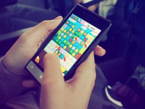 Ruke drže mobilni telefon dok prst dodiruje ekran sa igrom slagalicom sa šarenim bombonima